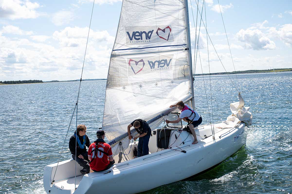 Elever arbejder med sejl og bådhåndtering i en Match 28-sejlbåd på Limfjorden under sejladsundervisningen på Venø Efterskole.